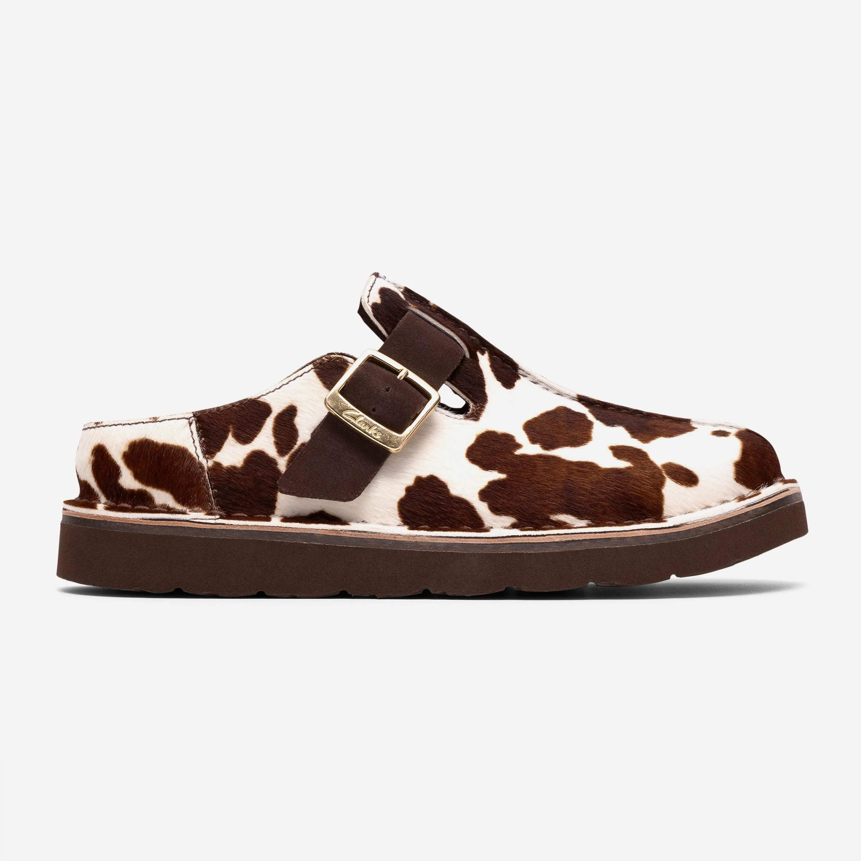 Profil extérieur de la mule Clarks Trek Mule Cow Print montrant la matière texturée à motif vache et la bride ajustable avec boucle dorée.