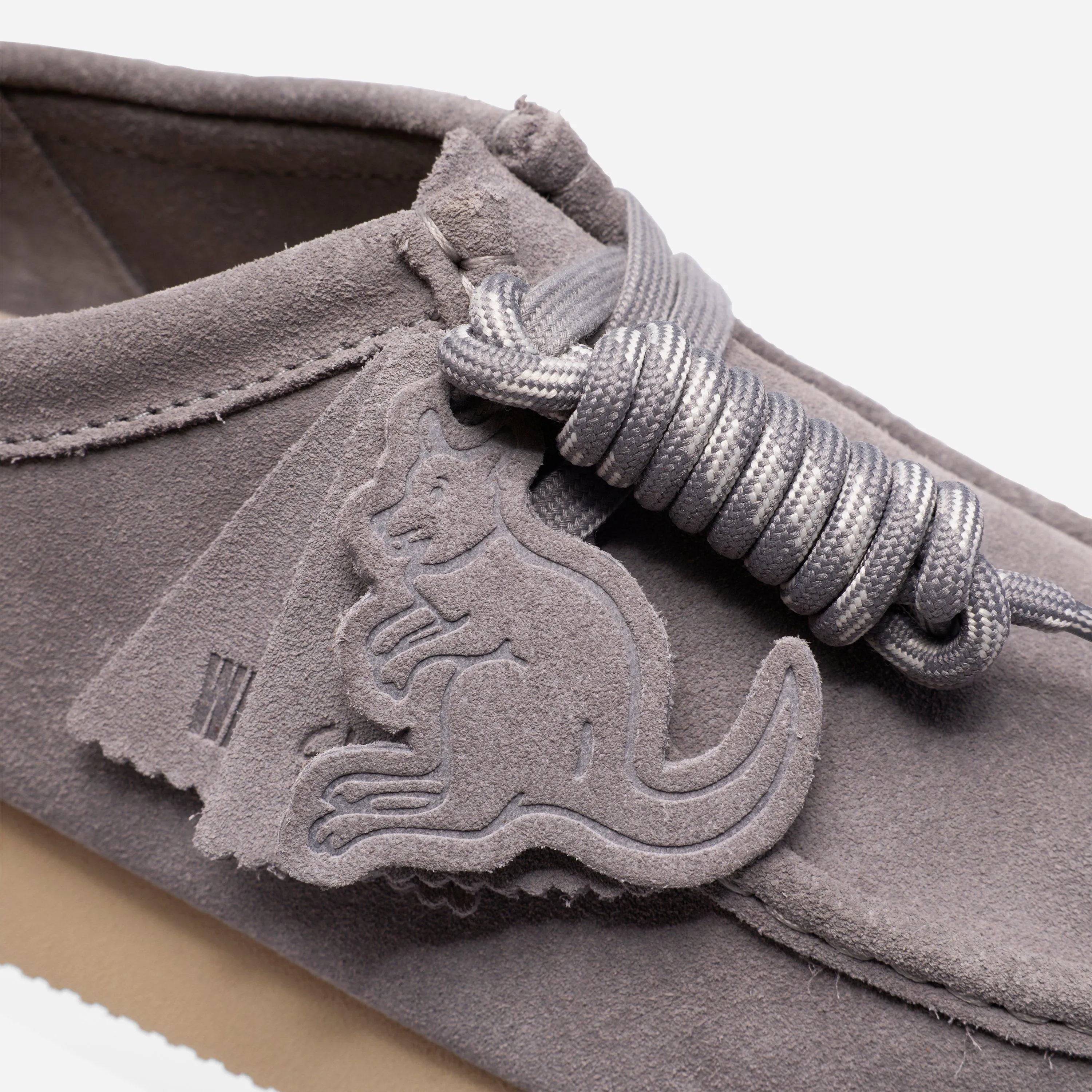 Détail de la texture du daim gris, des lacets épais et du badge kangourou exclusif de l'édition Wallabee Day.