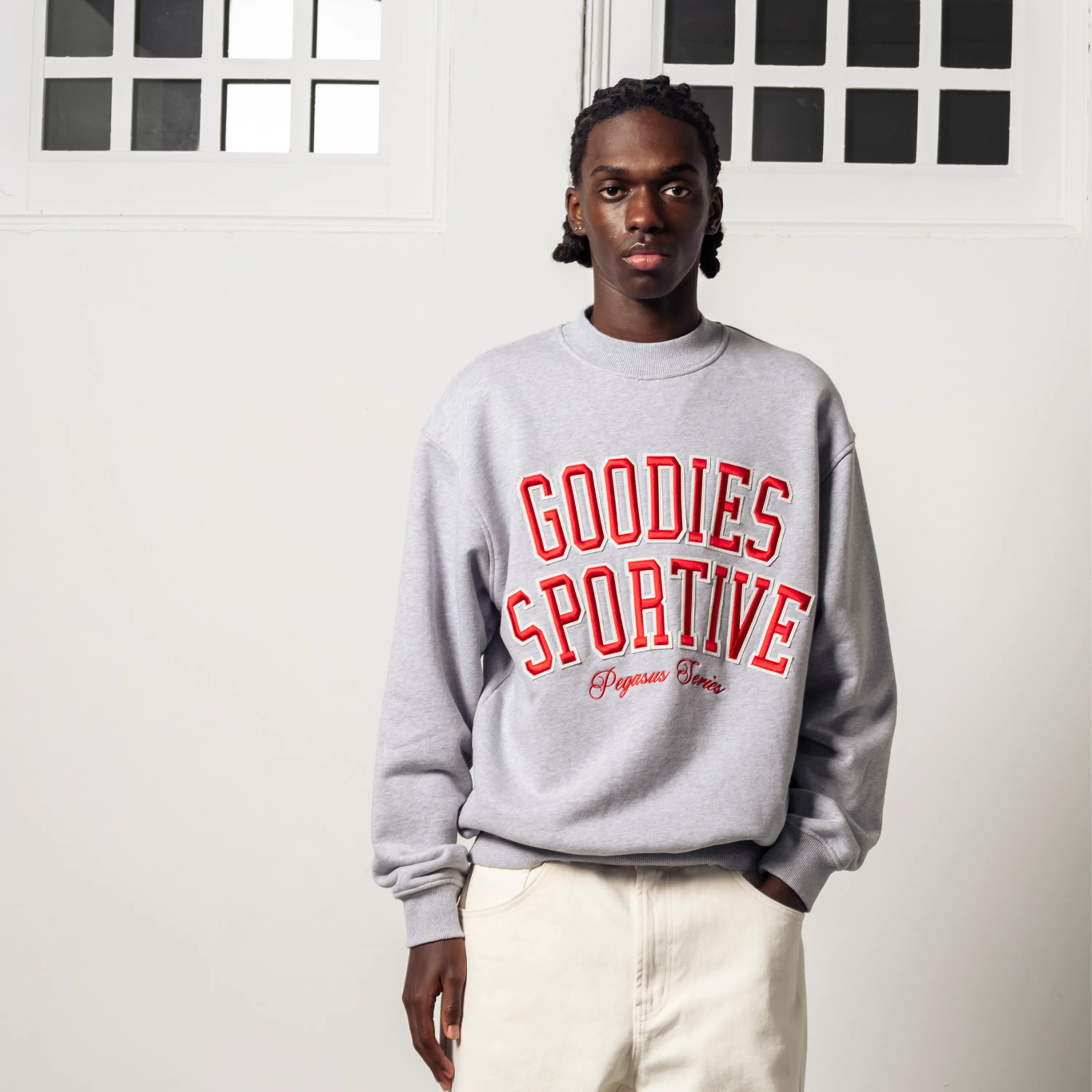 Man wearing a grey Goodies Sportive sweatshirt with a red logo and a boxy cut.