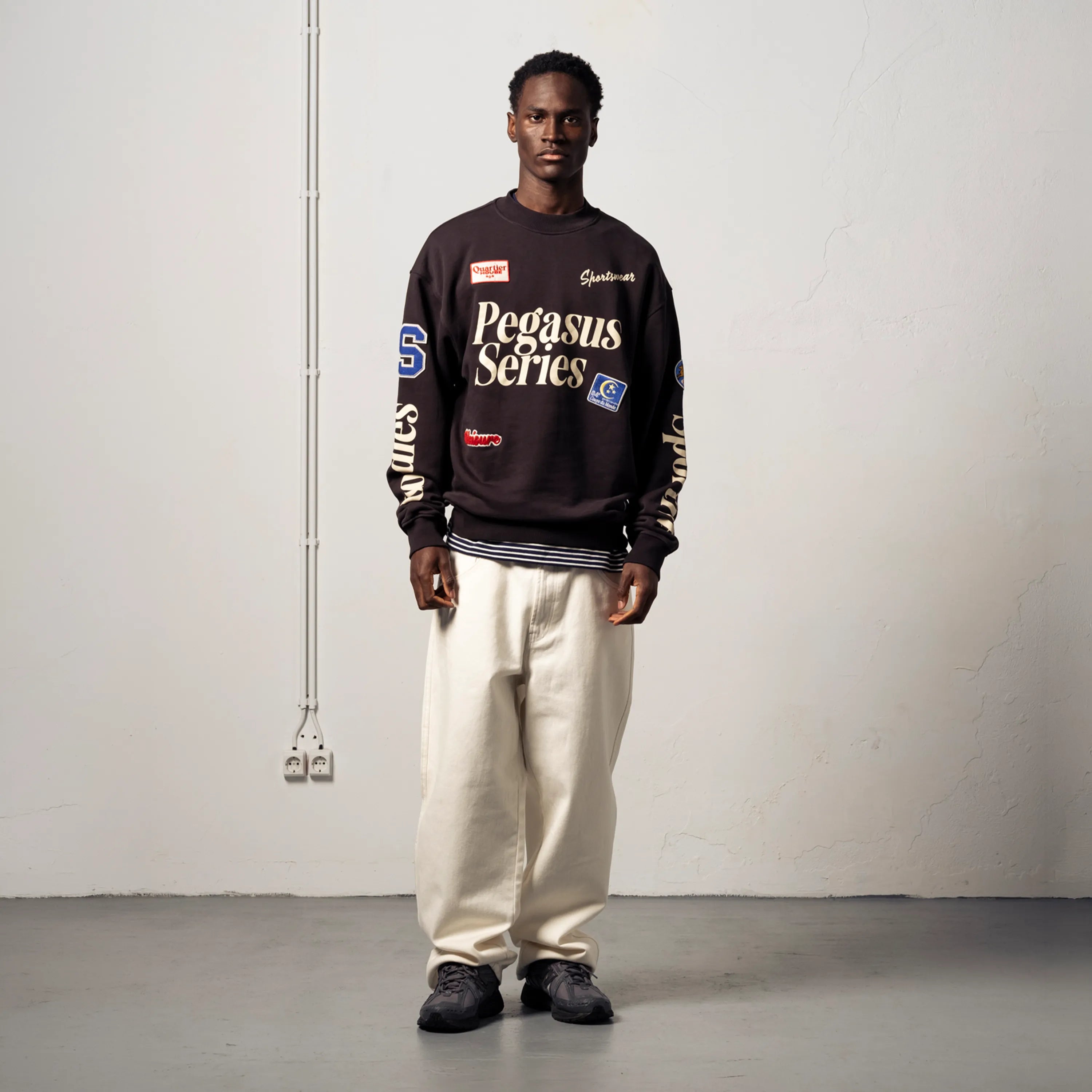 Man wearing a black boxy Goodies Sportive sweatshirt with white trousers.