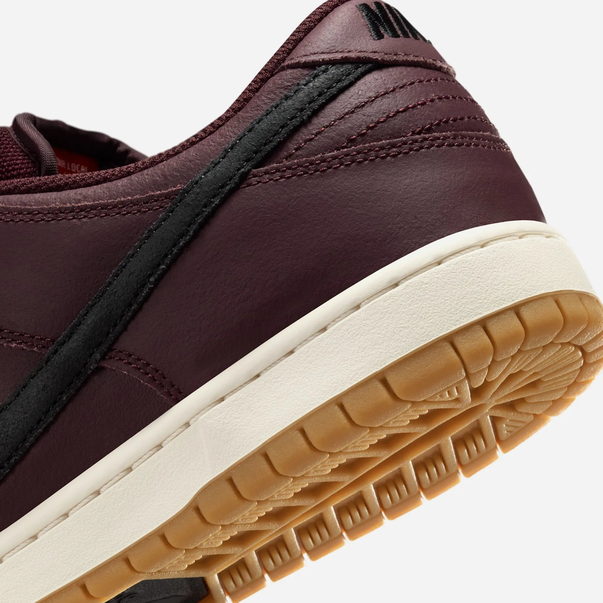 Detail of the black leather and burgundy grained leather Swoosh on Nike SB Dunk.