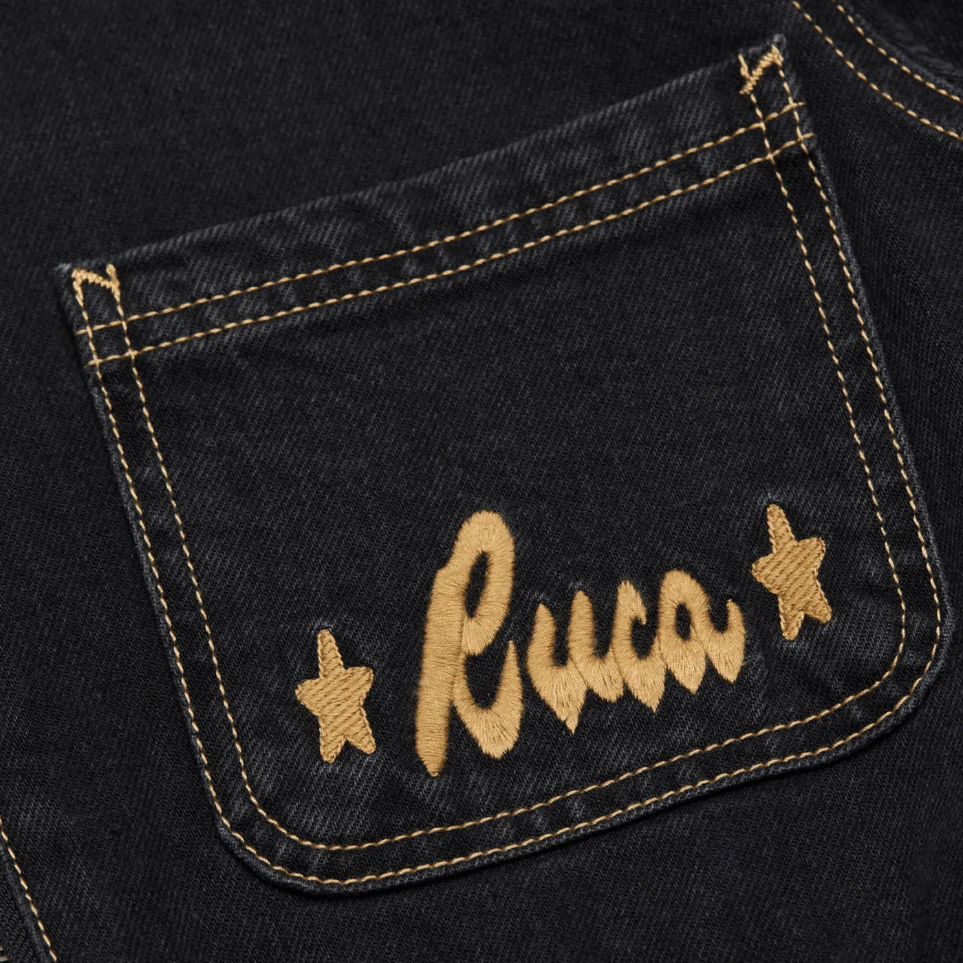Close-up of the chest pocket showing the gold Rvca embroidery on the Washed Black jumpsuit