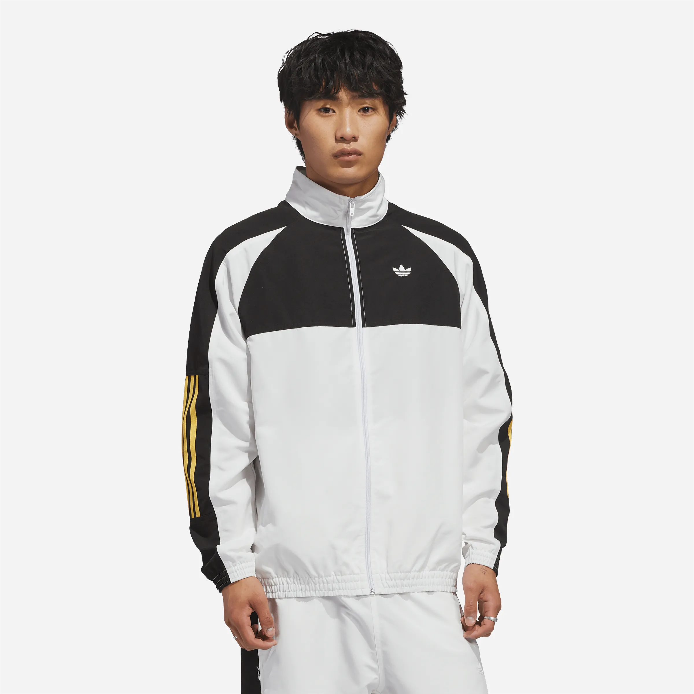 Homme en tenue skate avec veste Adidas Gatsele blanche et bandes jaunes.