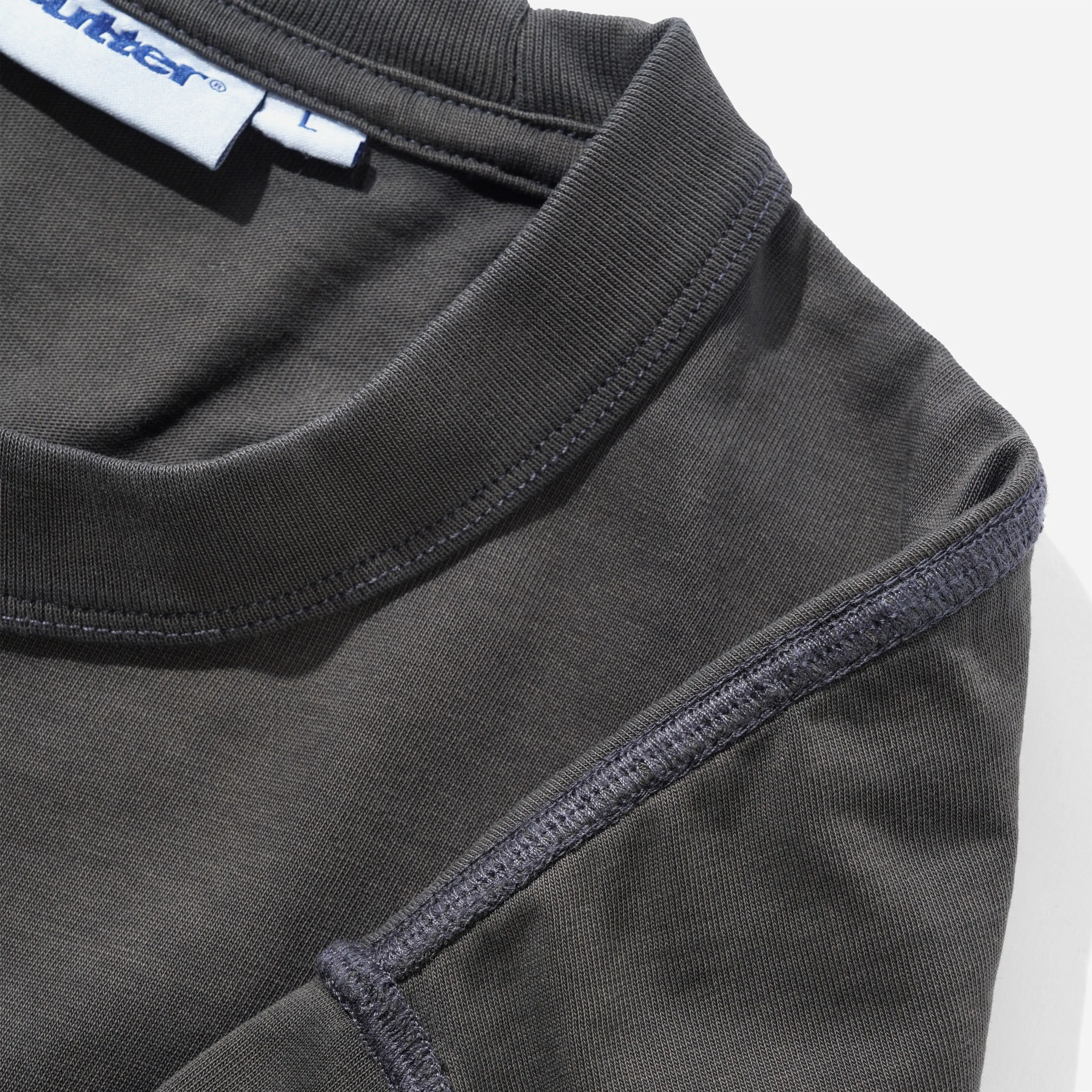 Gros plan sur les coutures apparentes cover stitch sur l'épaule et le col nervuré du t-shirt gris vintage Butter Goods.