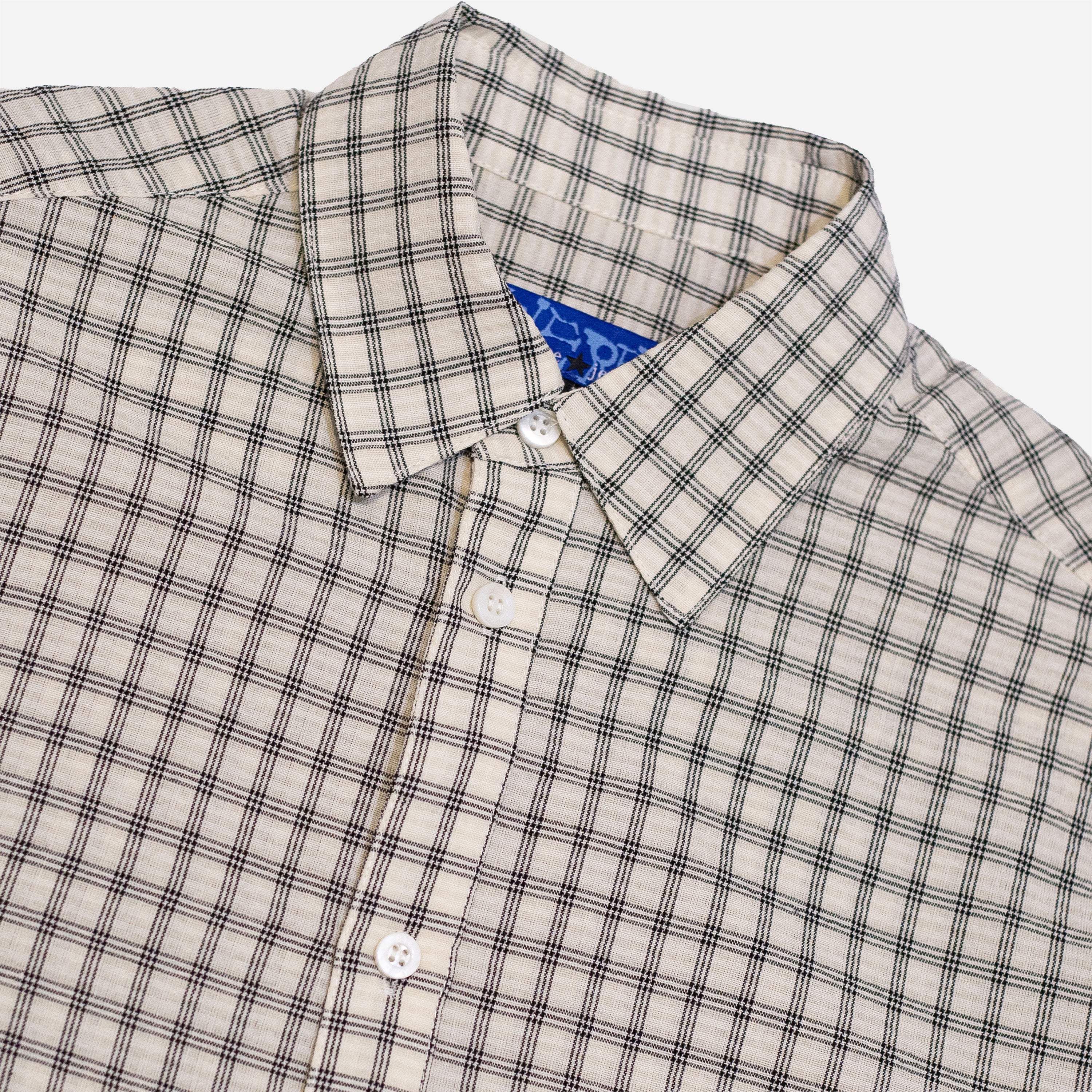 Détail du col de la chemise à manches longues à carreaux avec un patch logo papillon noir et blanc Bye Jeremy.