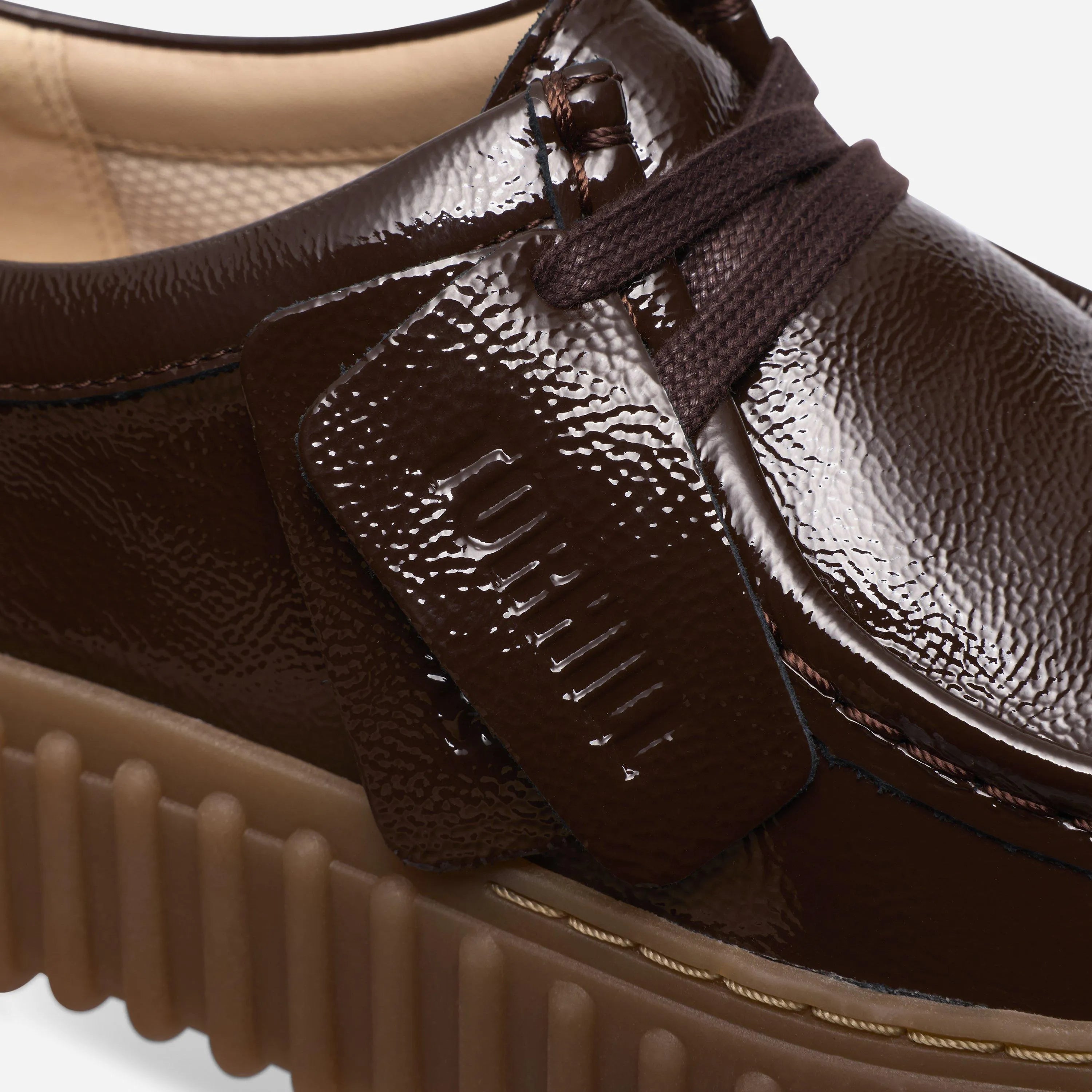 Close up on the laces, glossy brown patent leather, and the two embossed fobs stamped with Clarks and Torhill.