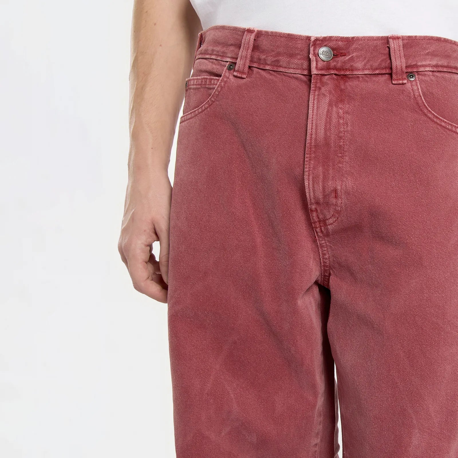 Zoom sur le tissu denim sergé rouge délavé et les rivets métalliques.