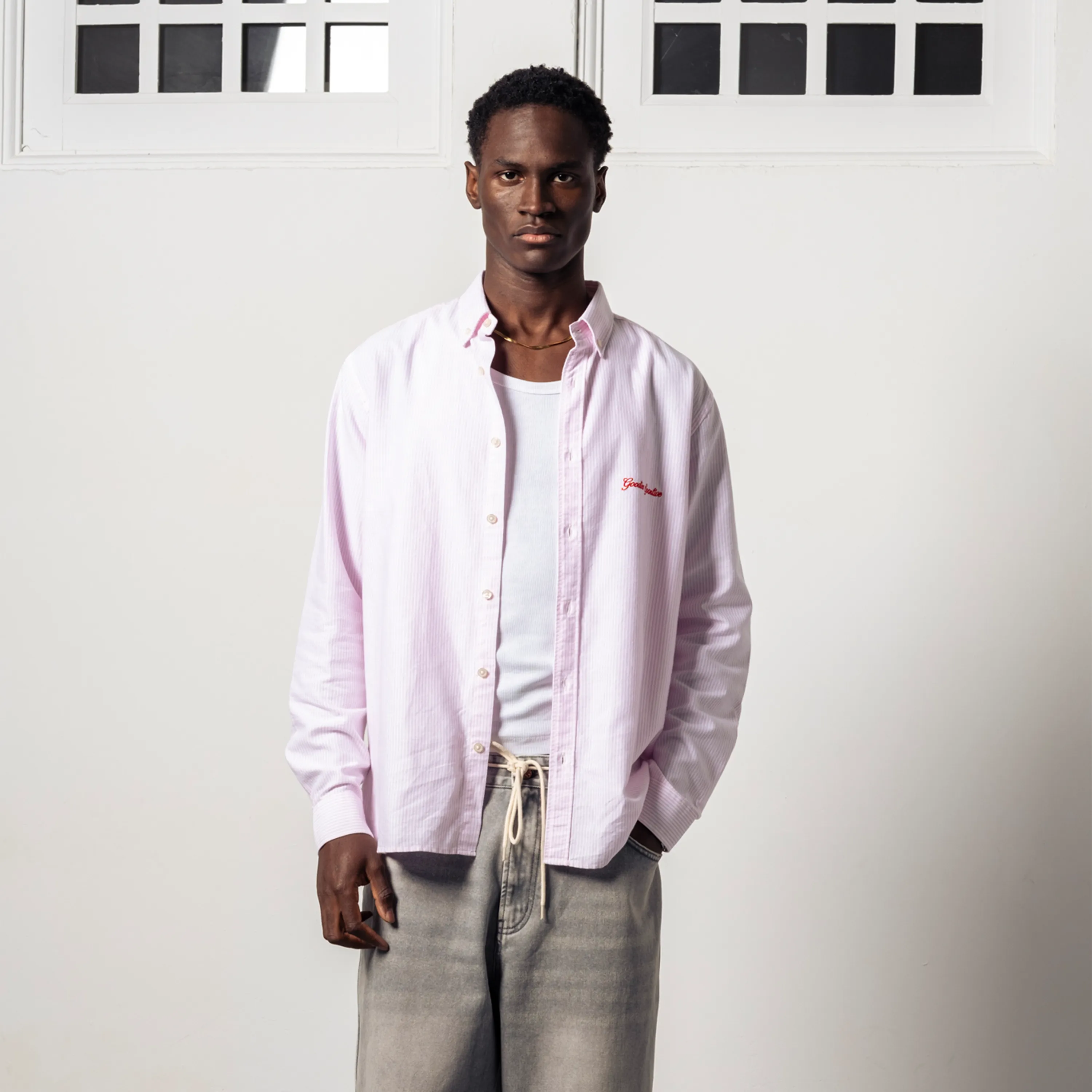 Man wearing a pink Oxford shirt open over a white vest.