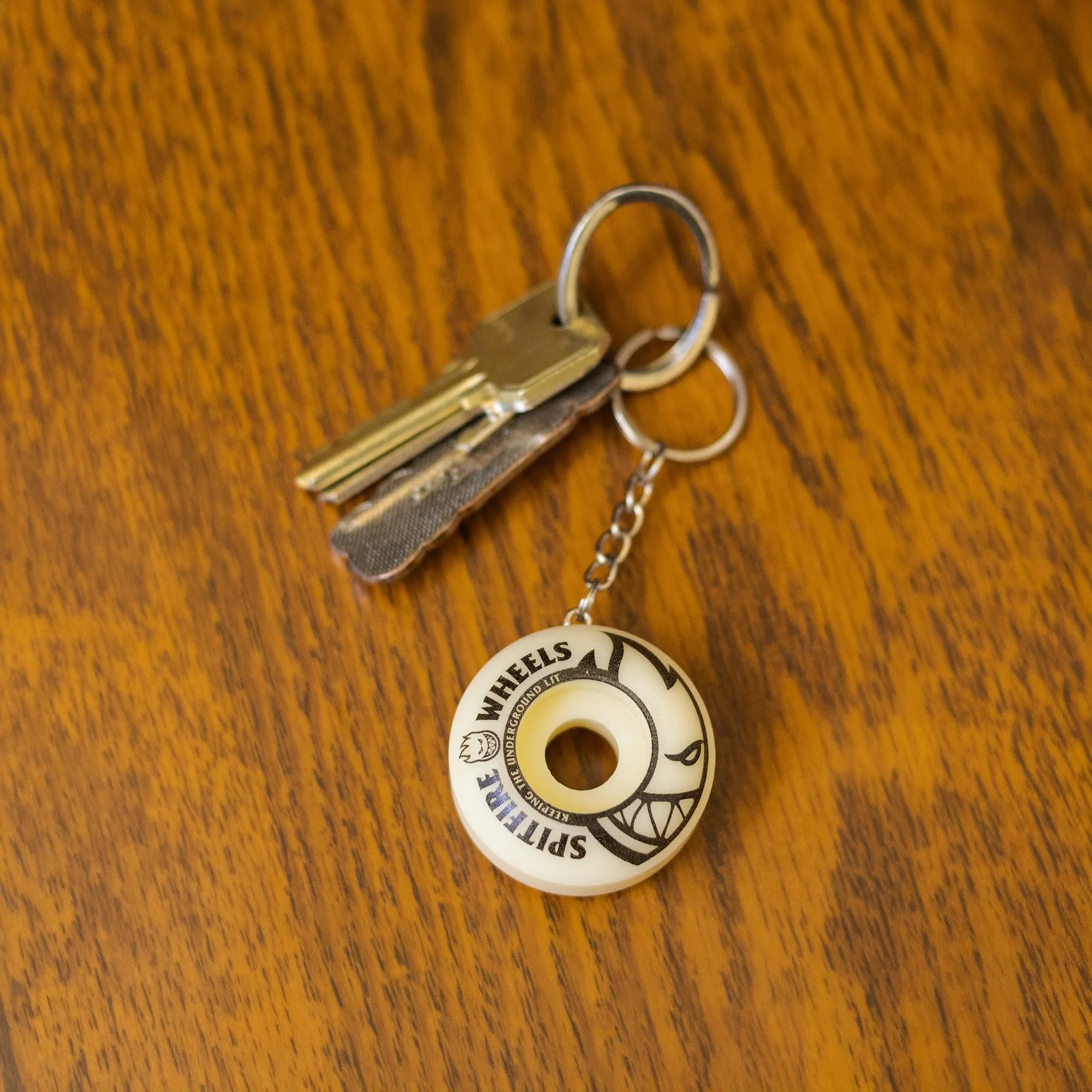 Spitfire skateboard wheel keyring attached to a set of keys on a wooden table.