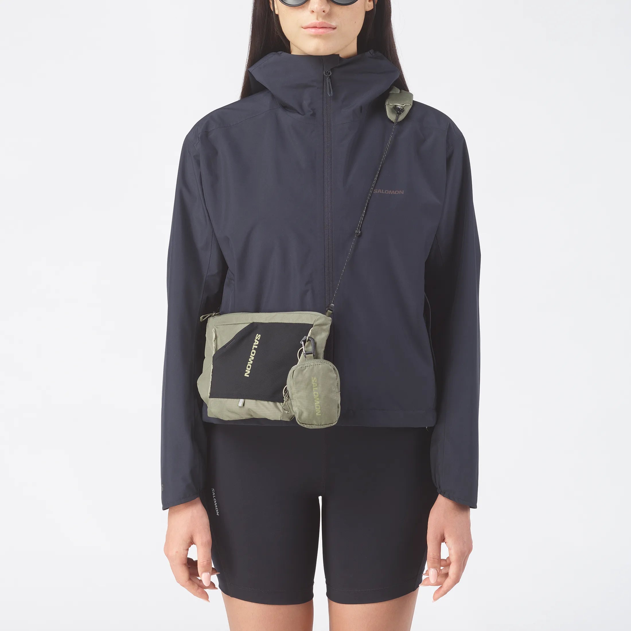 Femme portant la sacoche Salomon Deep Lichen Green en bandoulière sur veste noire.