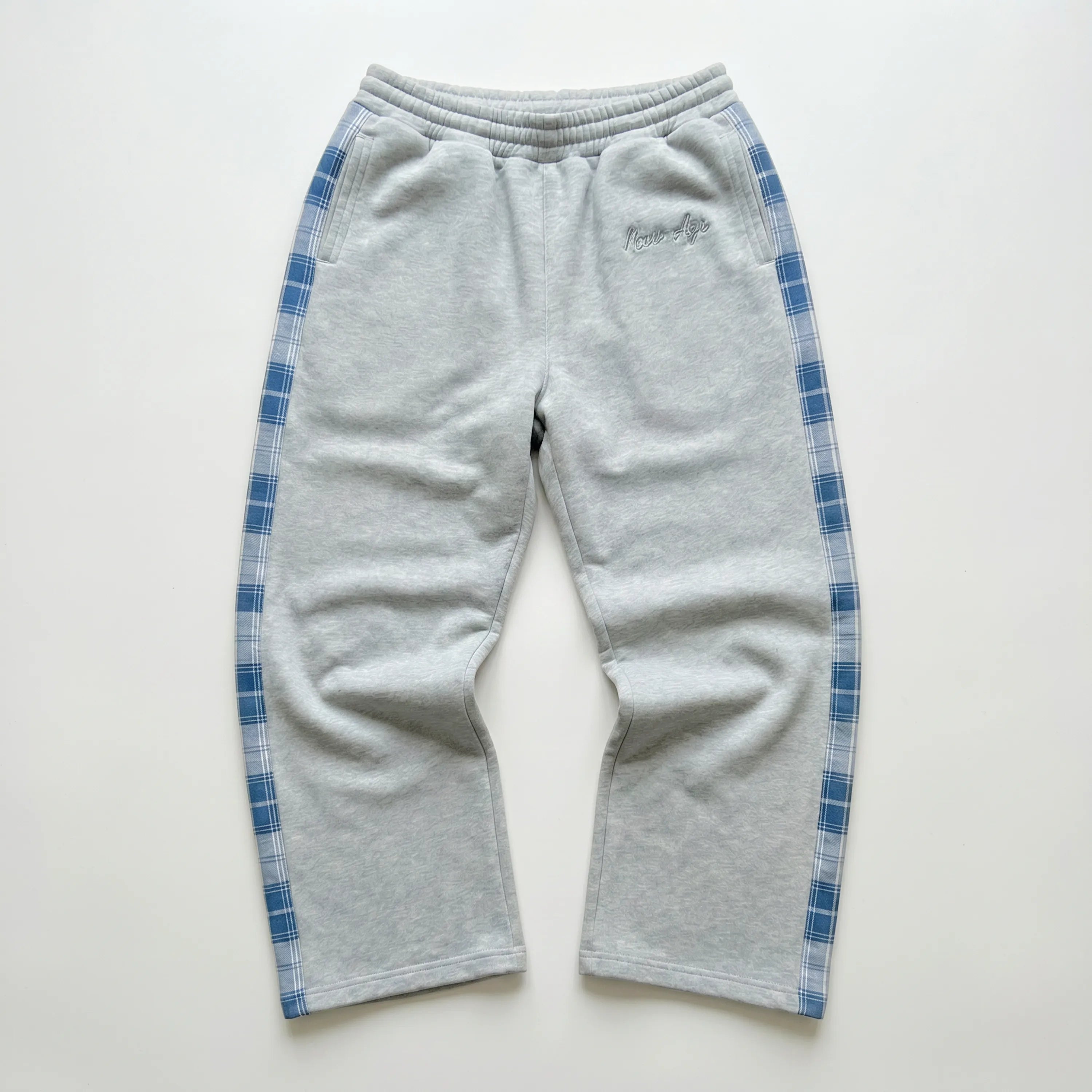 Pantalon de survêtement Maison New Age gris avec bandes à carreaux bleues.