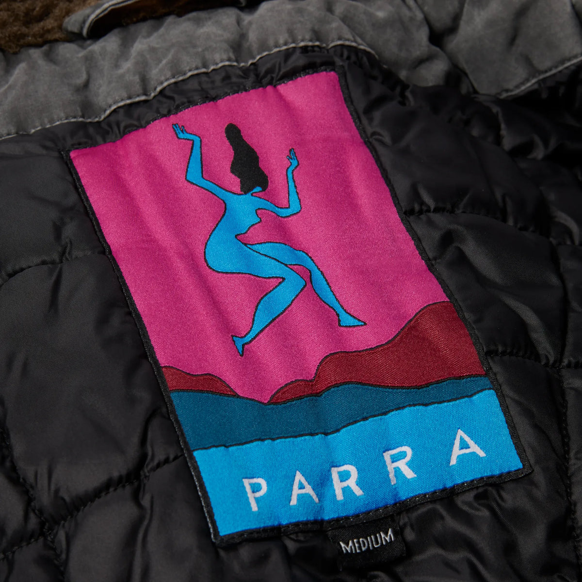 Zoom sur la doublure matelassée et la grande étiquette tissée artistique de la veste By Parra noire.